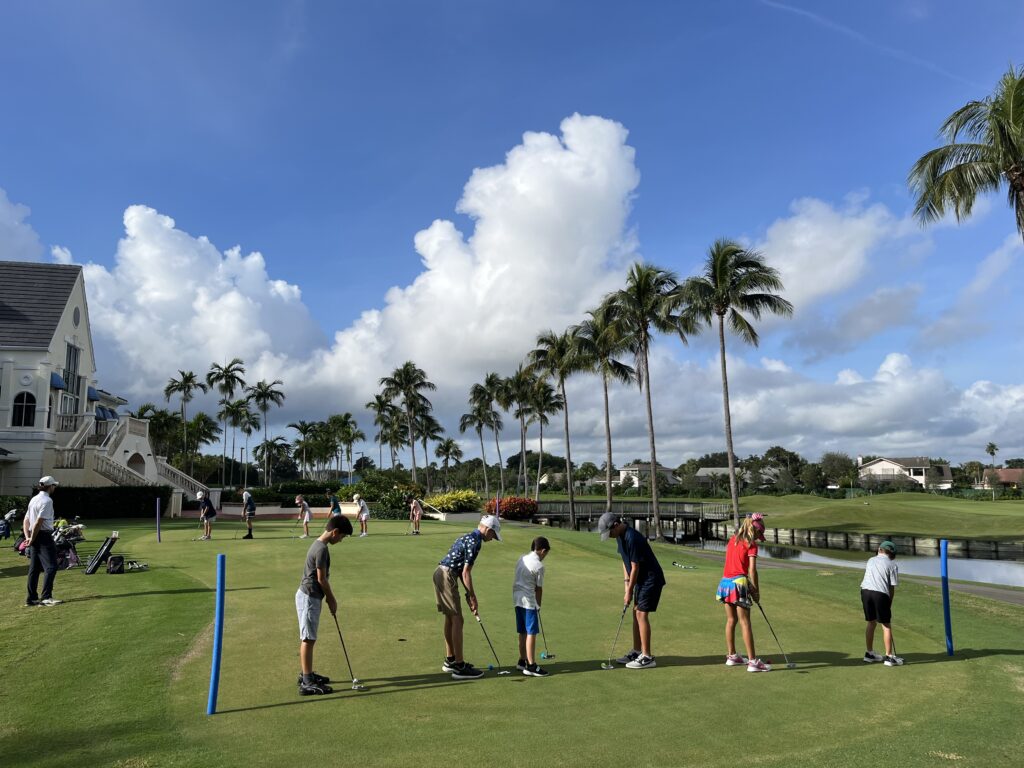 Children playing golf on a sunny day with palm trees and blue sky.