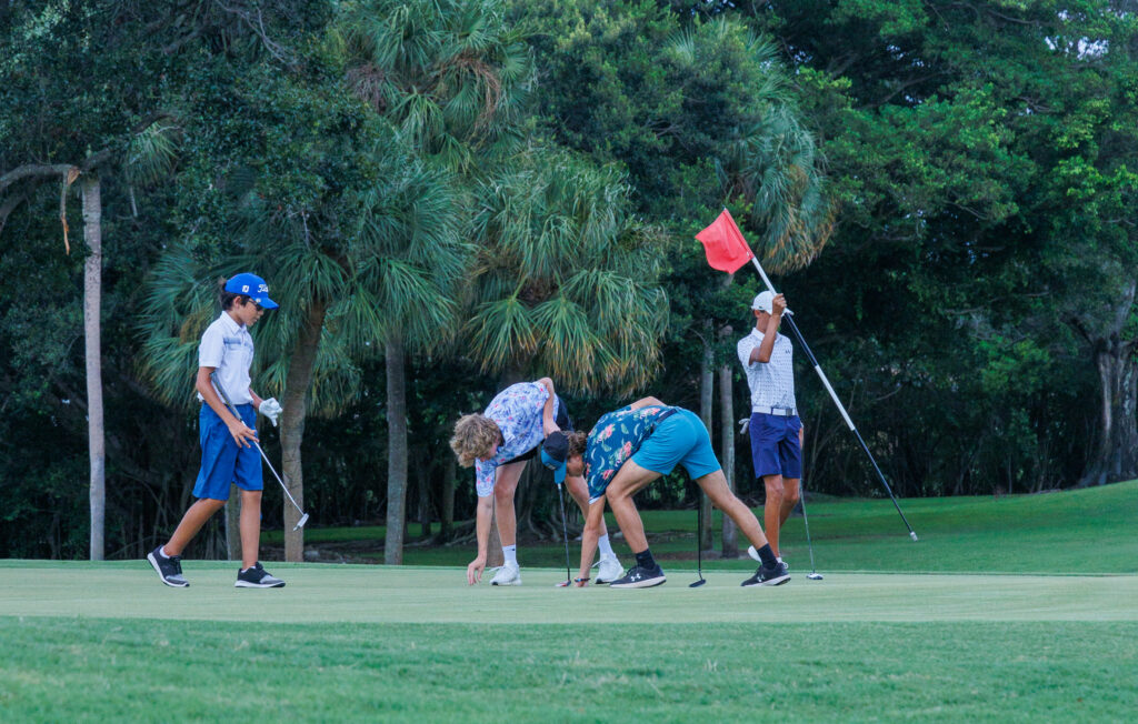 Golf players preparing to putt on a green near a forest.