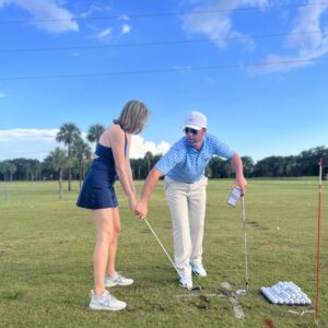 Two people practicing golf swings on a sunny day at a golf course.