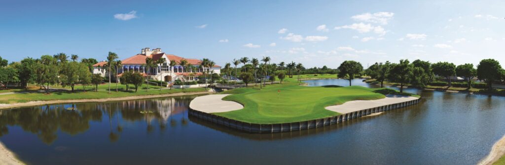 Scenic golf course with water hazards and palm trees under a blue sky.